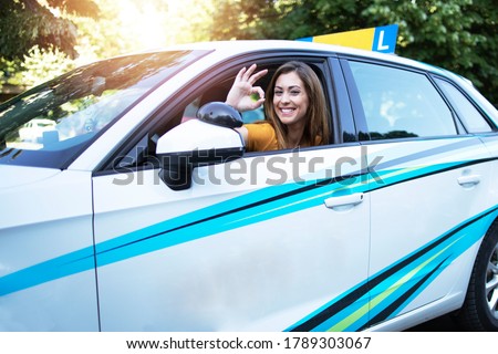 Car driving student showing okay gesture sign and sitting at vehicle driver position. Successful automobile driving classes.