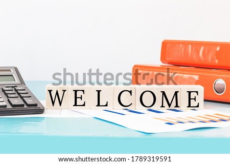 WELCOME text on wooden building blocks on top of office desk. Business finance meeting or workshop presentation and education concept. Calculator and binders. onboarding or induction. Copy space