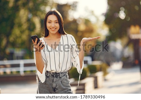 Portrait of beautiful brunette. Model in summer city. Girl standing with a mbile phone.