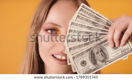 Portrait shot of woman with makeup covering half of the face with dollars. High quality photo