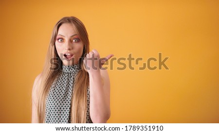 Fascinating long hair girl with amazed surprised face pointing to copy space. Isolated on yellow background. High quality photo