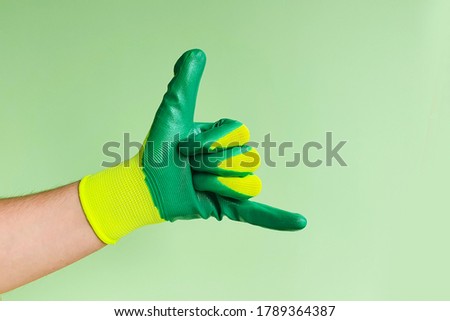 Male hand in a glove for working in the garden, vegetable garden. Hand gesture - Call me. Copy space