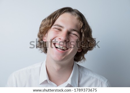 Smiling guy with long hair dressed in a white shirt on a white background