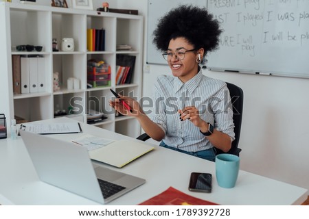 Learn with fun. Happy afro american female teacher sitting at her workplace and teaching English online, looking at computer screen and laughing. Focus on a woman. E-learning. Distance education Royalty-Free Stock Photo #1789392728