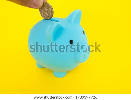 A hand putting a coin into a piggy bank. moneybox on a yellow background