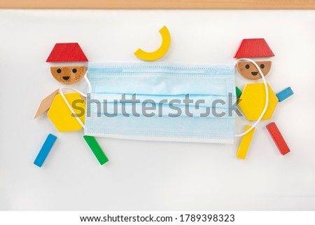 Stop corona pandemic with mouth and nose protection for school children concept. Face mask between children pictured from colourful magnetic wooden shape blocks