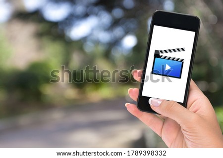 A woman holding a mobile phone with video service on the screen.