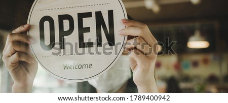Panoramic banner. waitress wearing protection face mask turning Open sign board reopen after coronavirus quarantine is over in cafe coffee shop ready to service, restaurant, food and drink concept