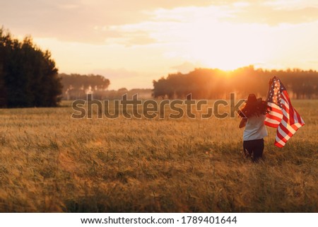 Woman farmer in the agricultural field with american flag on sunset.