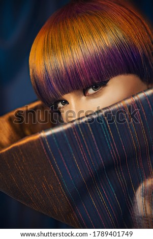 Young woman wearing a copper and blue long-sleeved and mock neck outfit, posing with colorful hair style