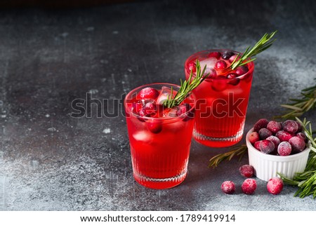 Cranberry drink cocktail with ice and rosemary on dark background, copy space