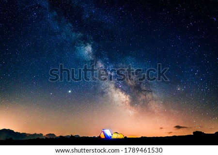 Tents glowing under the milky way at night. Camping in the mountains under the starry magical sky. 5 Billion Star Hotel. Royalty-Free Stock Photo #1789461530