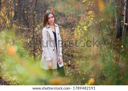 Beautiful slender girl in a raincoat in the autumn forest at sunset. Warm light. Yellow and red foliage