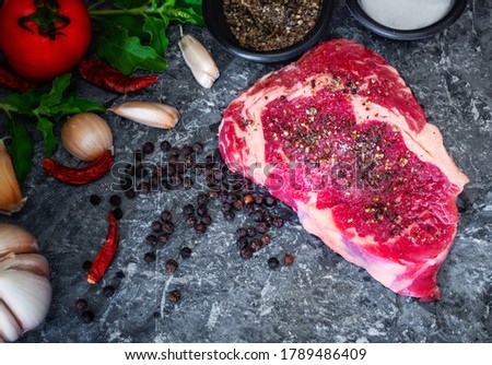 The picture of fresh raw rib eye steak of beef on stone dish with salt, pepper,garlic,tomato,and  basil garnish in a simple style.
