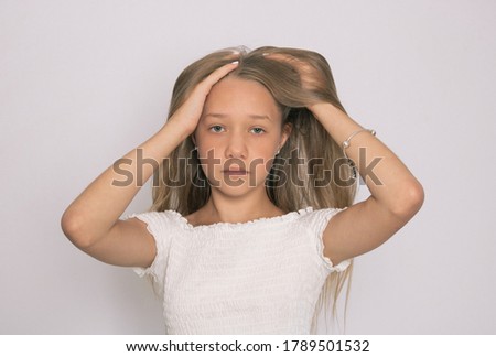 A girl on a gray background in a white T-shirt looks at the photographer. Both hands run through the hair
