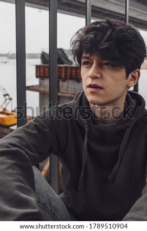 a young guy of Eastern appearance with black hair and a handsome expressive face poses in a Park against the background of trees and architecture. High quality photo