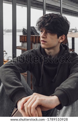 a young guy of Eastern appearance with black hair and a handsome expressive face poses in a Park against the background of trees and architecture. High quality photo