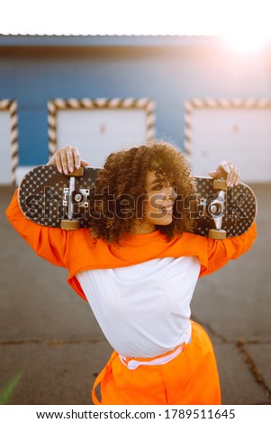 Beautiful African  American woman posing with a skateboard. Hipster woman with curly hair with skateboard at sunset. Fashion lifestyle.