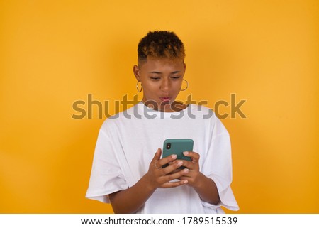 Portrait of crazy impressed afro american woman  isolated shine color background use cell phone reads incredible news on social media information stare, screams wow omg wear stylish outfit