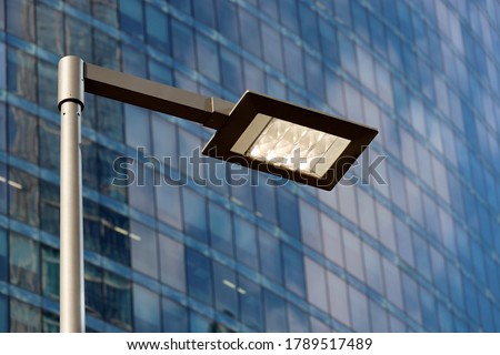LED street lamp post glowing on skyscraper background. Modern led lights in city, saving of electrical energy Royalty-Free Stock Photo #1789517489