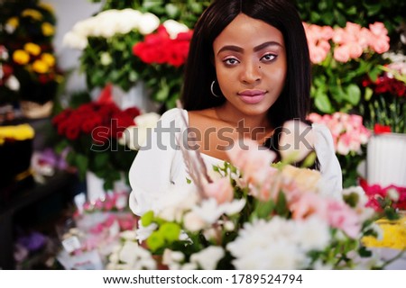 African american woman in white dress with bouquet flowers in hands at flower shop.