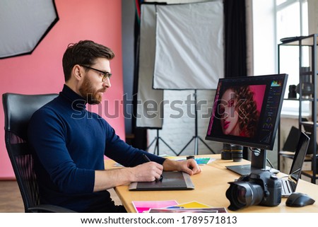 Retouching images in special program.Portrait of graphic designer working in office with laptop,monitor,graphic drawing tablet and color palette.Retoucher workplace in photo studio.Creative agency.