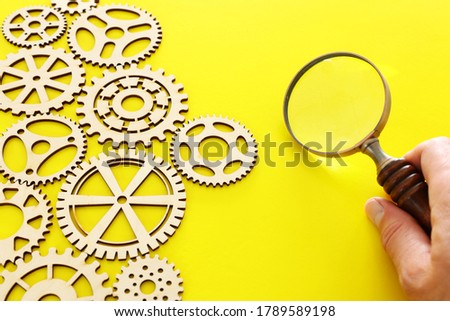hand placing a magnifying glass over set of gears mechanism