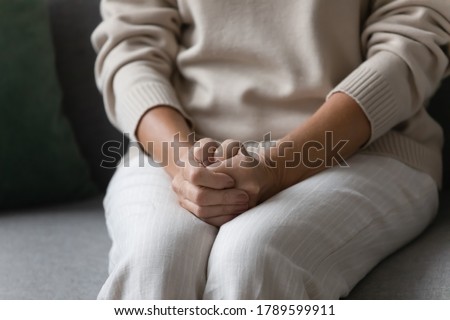 Close up image elderly woman feels nervous anxious or lonely put clenched hands on laps sitting on couch indoors. Older patient of nursing home, senile diseases and geriatric, declining years concept Royalty-Free Stock Photo #1789599911