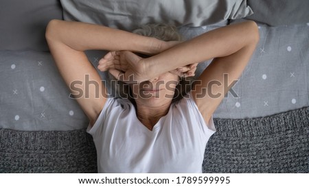 Top view aged woman lying on bed woke up at night due noisy neighbors. Mature female cover face with hands suffers from insomnia sleep disorder, has restless obsessive thoughts keep her awake concept Royalty-Free Stock Photo #1789599995