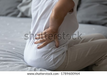 Elderly woman feels sudden strong backpain when got wake up in morning. Close up back view of old female put hand on lower back to reduce discomfort. Incorrect sleep night posture, rheumatism concept Royalty-Free Stock Photo #1789600964