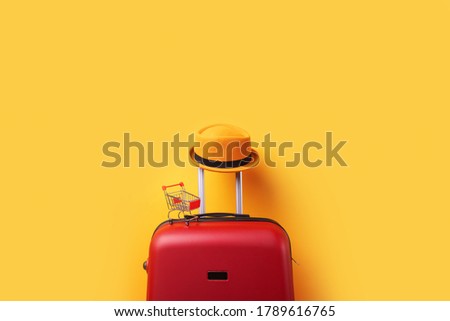 concept of shopping abroad, hat at suitcase with shopping cart over trend yellow background