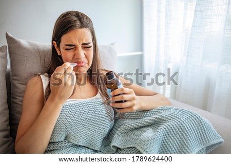 Cough syrup tastes awful. Young woman making a face of disgust at a spoon full of cough syrup. Sick woman sitting at the window of the house and drink the bitter medicine.  Royalty-Free Stock Photo #1789624400