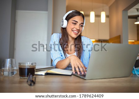Smiling girl student wear wireless headphone study online with skype teacher, happy young woman learn language listen lecture watch webinar write notes look at laptop sit in cafe, distant education Royalty-Free Stock Photo #1789624409