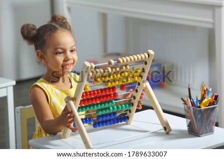 an african-american girl sits at a table and counts on an abacus and smiles Royalty-Free Stock Photo #1789633007