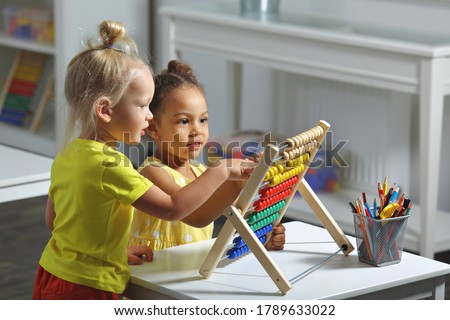 white and dark skinned children sit together at the table and count on the abacus and smiles Royalty-Free Stock Photo #1789633022