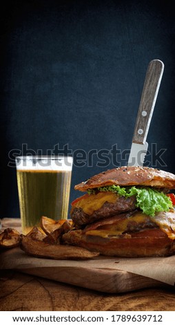 View of delicious burger and fries with glass of beer on wooden table