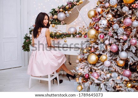 Merry Christmas and New Year. Cheerful womanl in white classic interior playing on a white piano against the background of a decorated Christmas tree.