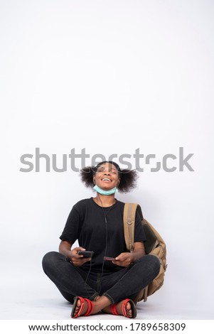 beautiful young african woman carrying a backpack, sitting legs crossed using her mobile phone and credit card, feeling satisfied