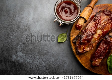 Delicious BBQ baby-back ribs with tangy sauce and a basting brush on black background, top view Royalty-Free Stock Photo #1789677074
