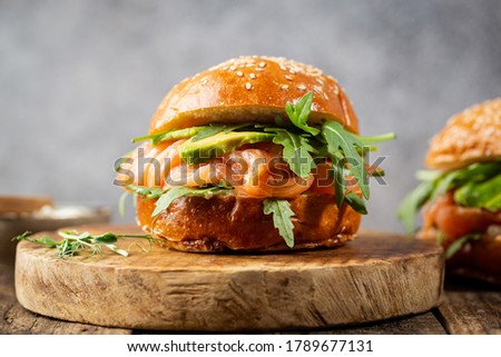 Burger sandwich with salmon, cream cheese, avocado and arugula on a light background, concept diet food, sandwich take away, healthy fast food