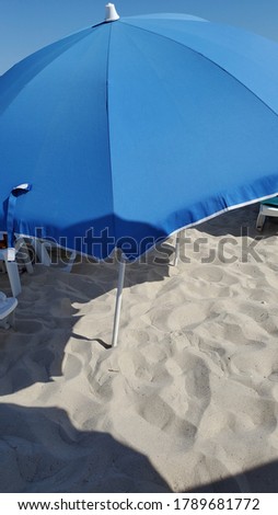 Blue sunshade on clear beach sand in sunny noon. Geometry of summer beach. Sea vacation background with copy space