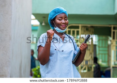 image of a black health professional wearing face mask under chin and stethoscope around neck,hands raised up for support and strength in covid-19 pandemic Royalty-Free Stock Photo #1789691888