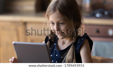 Happy little Caucasian girl look at tablet screen have fun play online application game on gadget, smiling small child kid study distant on internet on modern pad device, children technology concept