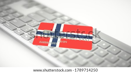Plastic bank card depicting flag of Norway on computer keyboard. Fictional numbers