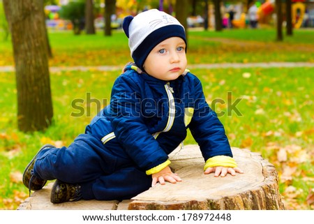 Lovely kid sitting on a stump and looks into the distance pensively