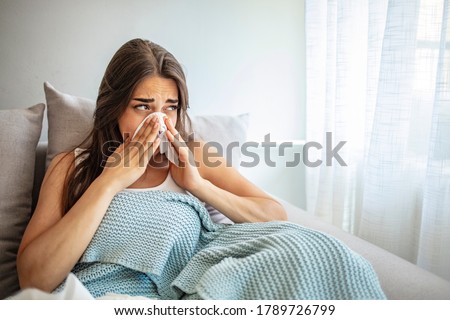 Woman Covered With a Blanket Lying in Bed With High Fever and a Flu, Resting at Living Room. She Is Exhausted and Suffering From Flu. Sick Woman With Runny Nose Lying in Bed. Girl Suffering From Cold 