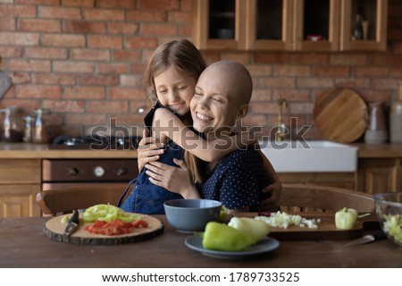Loving cute little girl child hug sick cancer patient bald mother cooking healthy food salad in kitchen together, caring small daughter embrace show love support to ill mom, feel grateful thankful Royalty-Free Stock Photo #1789733525