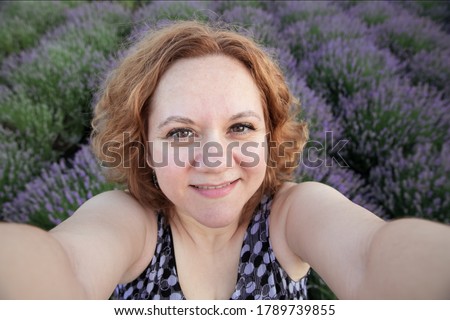 Joyful woman in lavender field looking at camera and smile. Adult woman taking a selfie in a purple lavender blossom meadow field on a holiday travel vacation.