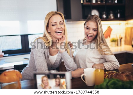 Happy mother and daughter with smartphone having breakfast and taking selfie at home kitchen
