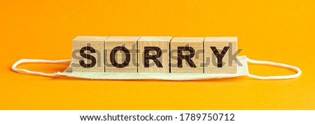 Sorry word written on wood block. Wooden block with words SORRY on wooden cubes, with the medical mask , health concept, yellow background. Medical concept